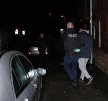 GLAA officer escorts suspect to vehicle at night