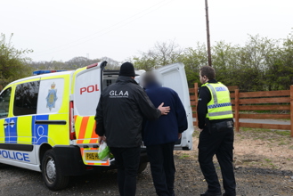 A GLAA worker escorting a suspect into a police van