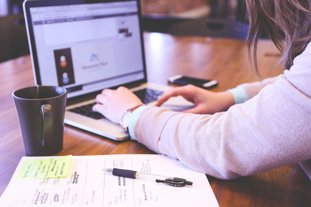 a woman typing on a laptop with a pen and paper next to her