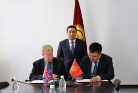 Two men sat at a table. One of them is signing a document